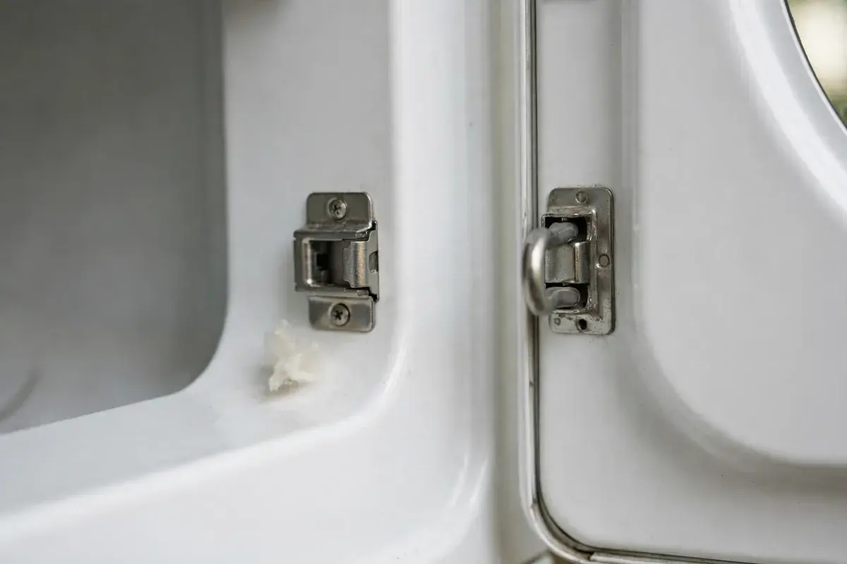 Dryer door latch catch and strike plate in close-up with a small tuft of lint