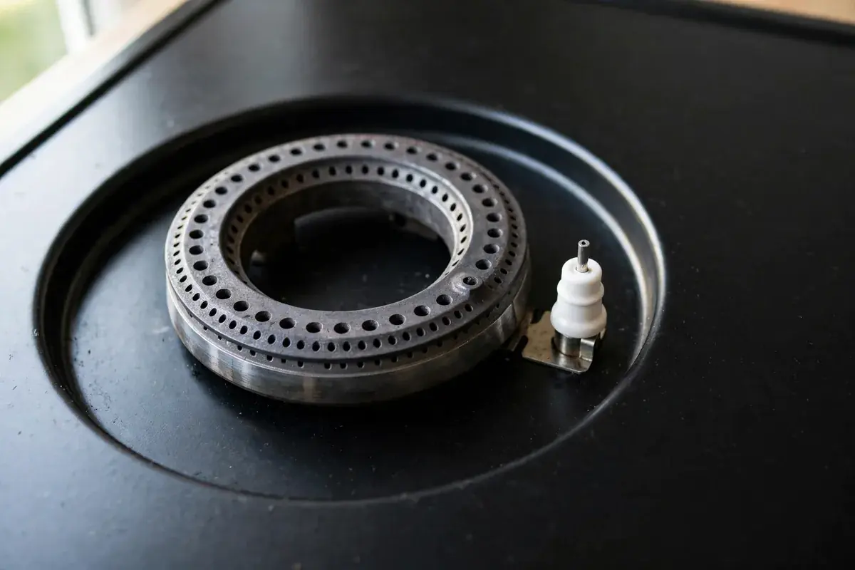 Gas burner head with the cap removed showing flame ports and igniter
